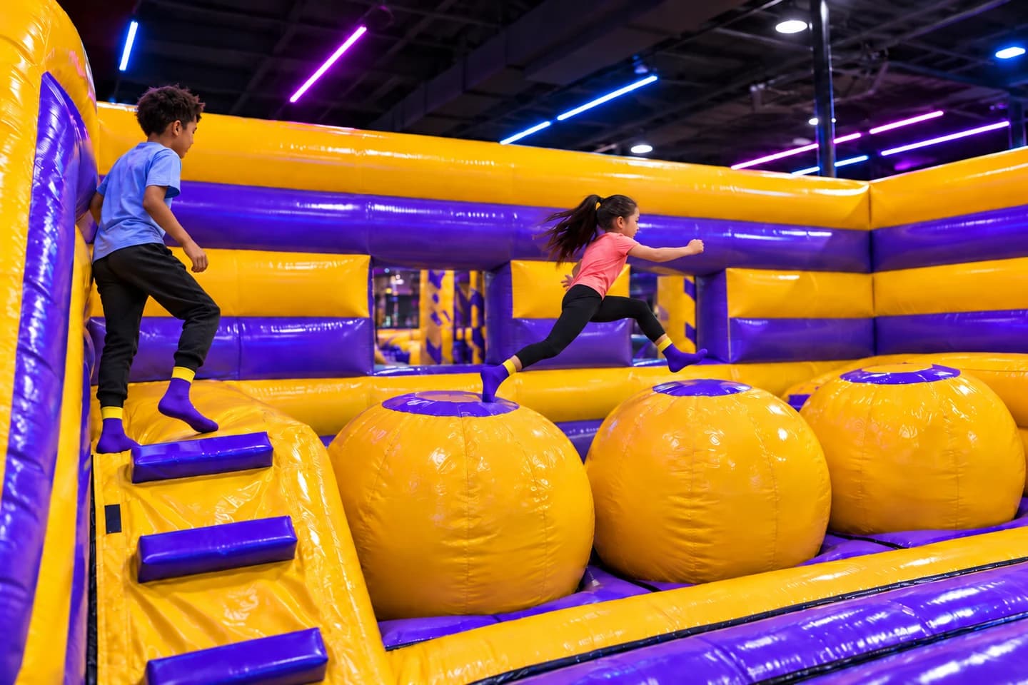 Children crossing large yellow inflatable ball obstacles at Super Llama Allen